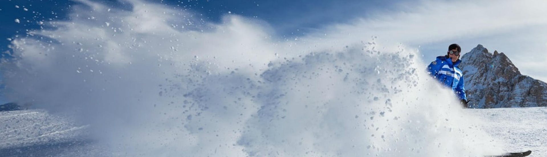 Un maestro di sci della scuola di sci Scuola di Sci Azzurra Cortina sta sciando lasciando una scia di neve bianca dietro di sé su una delle piste del comprensorio sciistico di Cortina d'Ampezzo, dove si tengono le lezioni di sci.