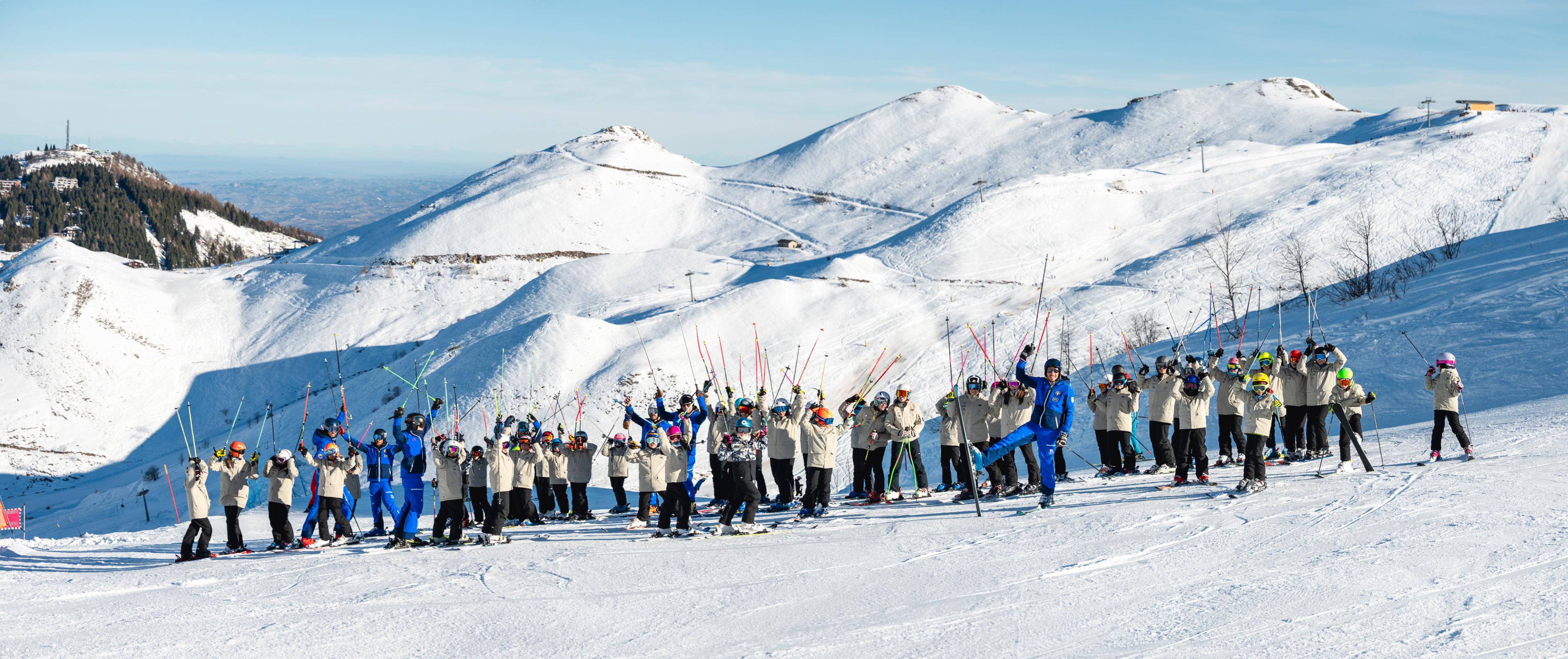 De ski- en snowboardleraren van Scuola di Sci e Snowboard Prato Nevoso met een besneeuwde berg op de achtergrond.