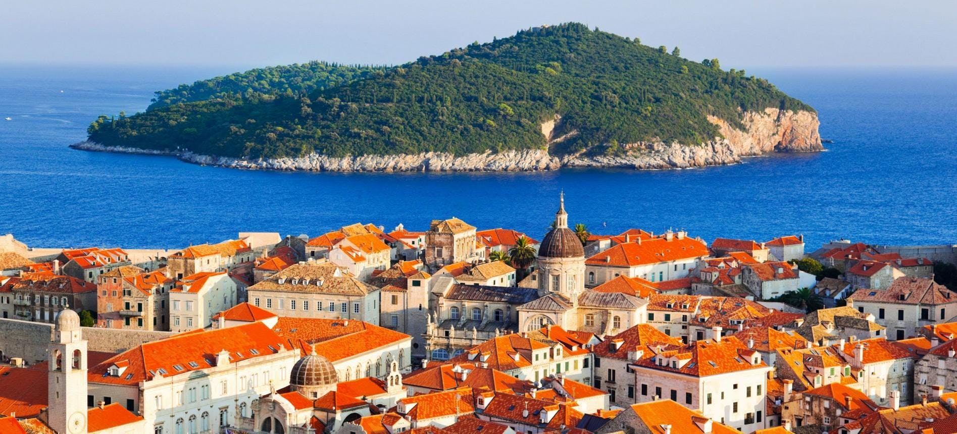 Select Dubrovnik Background Aerial image of Dubrovnik, showing the rooftops of the old town and an island in the background.