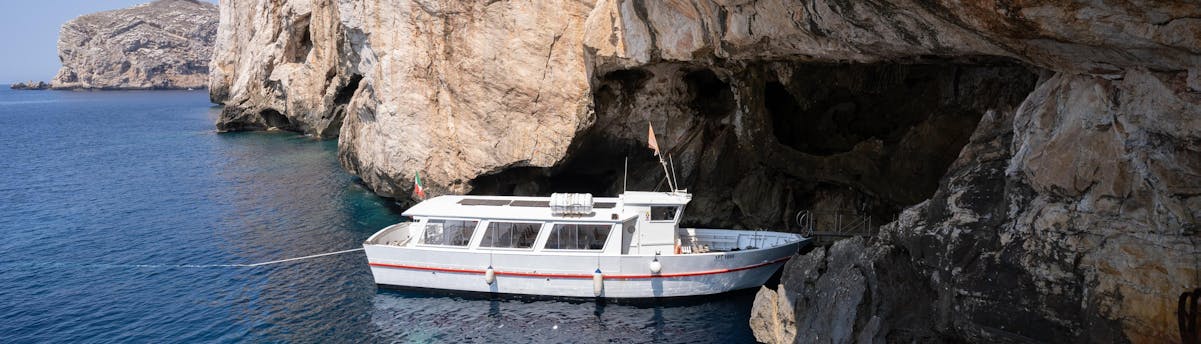 Tour in barca alla Grotta di Nettuno SEM Hero Una barca entra nella Grotta di Nettuno, lungo le scogliere della Sardegna.