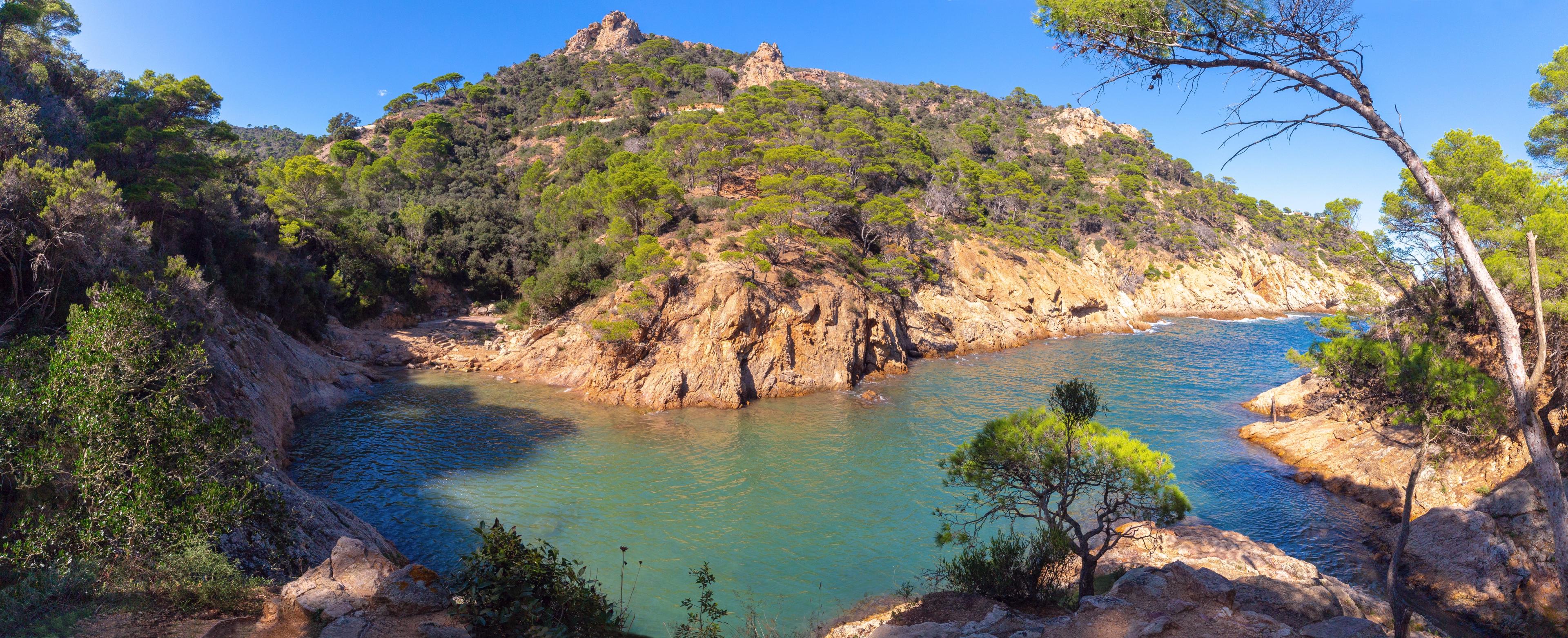 Rocky cliffs along the coastline of Cala Bona under a clear sky.