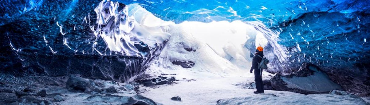Glacier and Ice Cave Tours SEM Hero 3 Un hombre explora una cueva de hielo, rodeado de brillantes paredes de hielo azul.