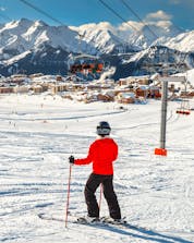 A skier is taking a break from their ski lessons to enjoy the view of the ski resort of Alpe d'Huez from the ski slope.