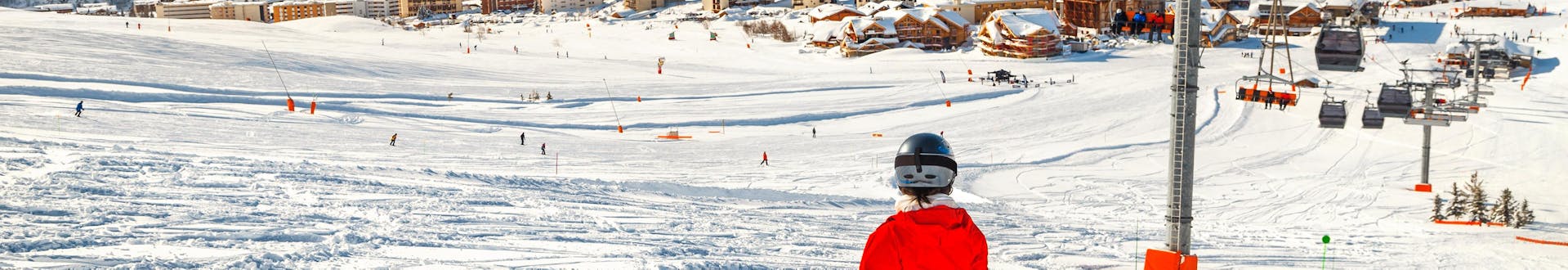Ein Skifahrer legt bei seinem Skikurs eine Pause ein um den Ausblick auf das Skigebiet Alpe d'Huez von der Piste aus zu genießen.