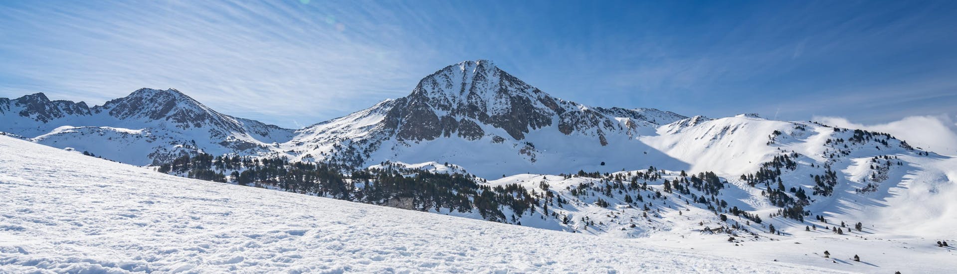 Imagen del sol brillando sobre las montañas nevadas en Baqueira, estación de esquí española done las escuelas de esquí locales ofrecen clases de esquí a los visitantes que quieren aprender a esquiar.