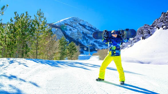 Uno snowboarder sta sorridendo alla fotocamera su una pista soleggiata del comprensorio sciistico di Campo Felice, dove è possibile scegliere tra un'ampia gamma di corsi di sci e snowboard offerti dalle scuole di sci locali.