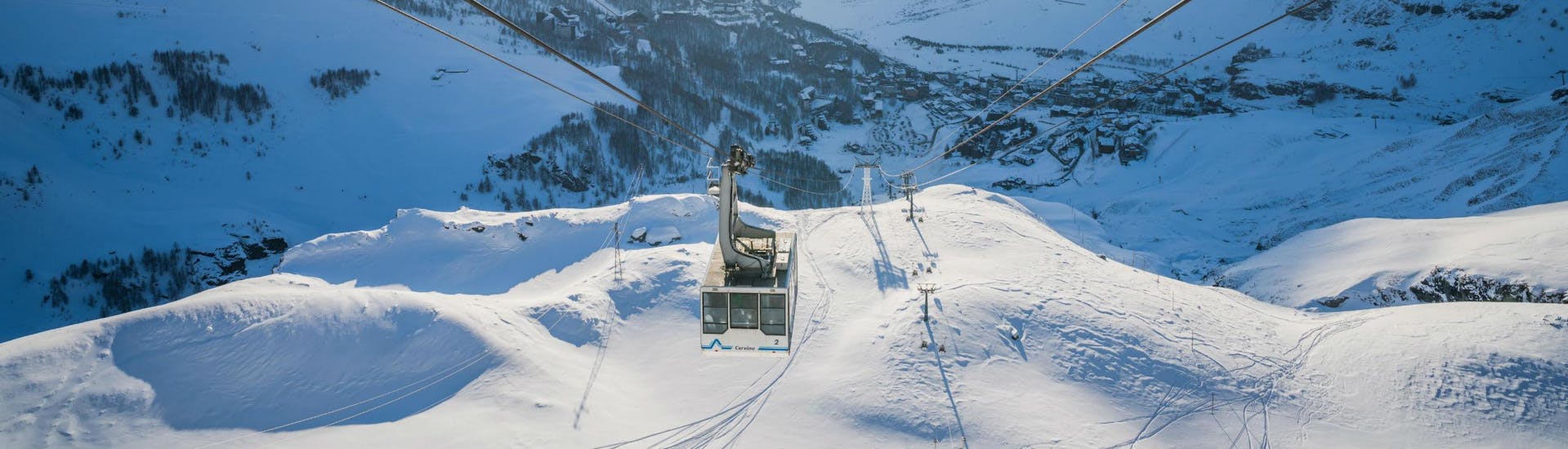 Una funivia sta risalendo i pendii del comprensorio sciistico di Cervinia, dove i turisti possono imparare a sciare grazie alle lezioni di sci impartite dalle scuole di sci locai.