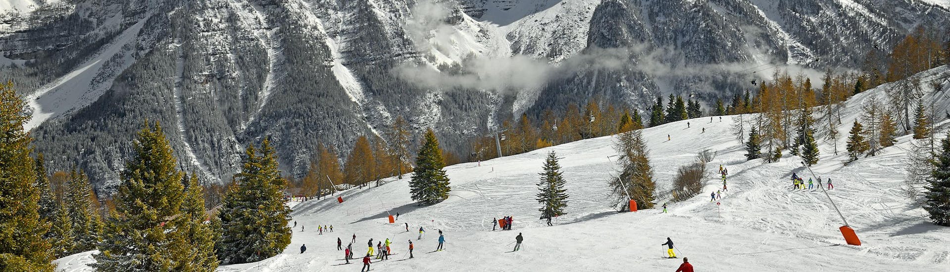 Una vista panoramica del paesaggio montano mentre le persone imparano a siare grazie alle lezioni di sci di una scuola di sci locale presso Trentino.