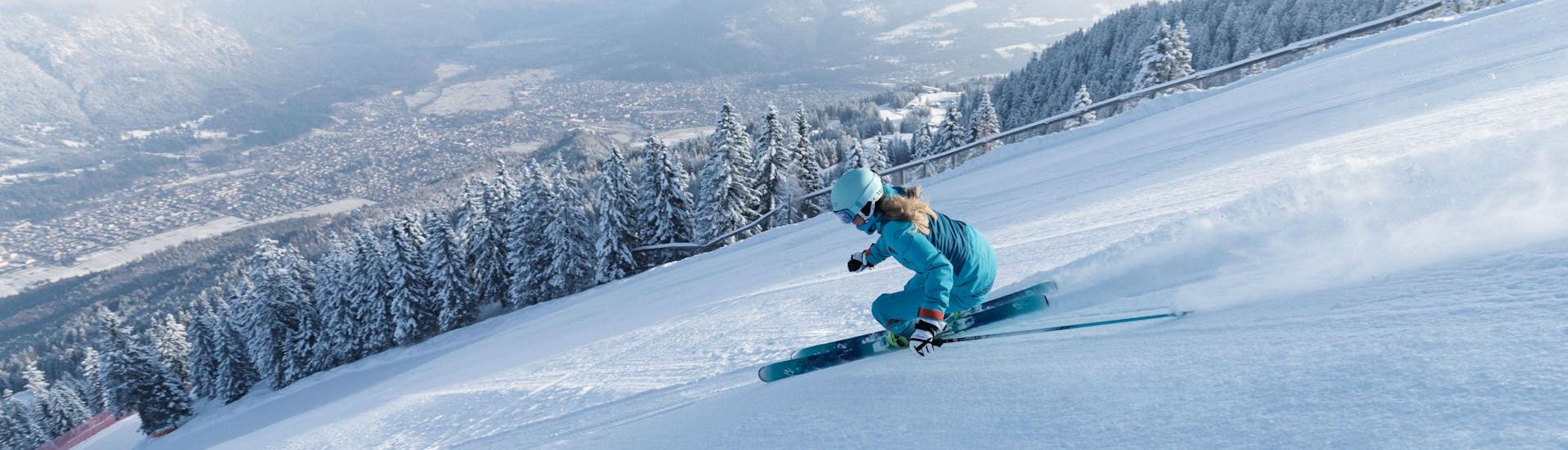 A female skier is speeding down a perfectly prepared slope overlooking the ski resort of Garmisch-Classic, where local ski schools offer a broad selection of ski lessons. (c)Bayerische Zugspitzbahn Bergbahn AGfendstudios.com