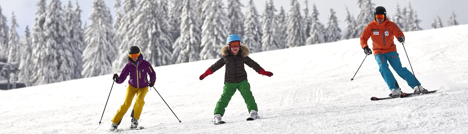 Eine Familie bestehend aus zwei Erwachsenen und einem Kind beim Skifahren am Großen Arber, einem beliebten deutschen Skigebiet in dem man bei einer der örtlichen Skischulen einen Skikurs buchen kann.