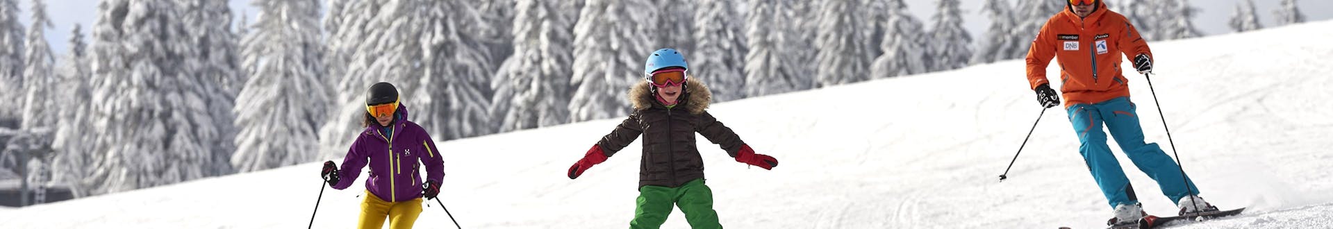 Eine Familie bestehend aus zwei Erwachsenen und einem Kind beim Skifahren am Großen Arber, einem beliebten deutschen Skigebiet in dem man bei einer der örtlichen Skischulen einen Skikurs buchen kann.