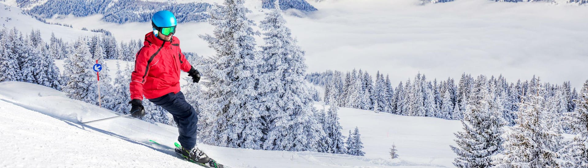 A skier is skiing down a ski slope with fresh powder snow and a stunning view of the surrounding Alps in the Kitzbühel area, where local ski schools offer a variety of ski lessons for anyone who wants to learn to ski.