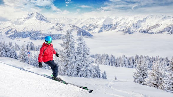 A skier is skiing down a ski slope with fresh powder snow and a stunning view of the surrounding Alps in the ski resort of Kitzbühel, where local ski schools offer a variety of ski lessons for anyone who wants to learn to ski.