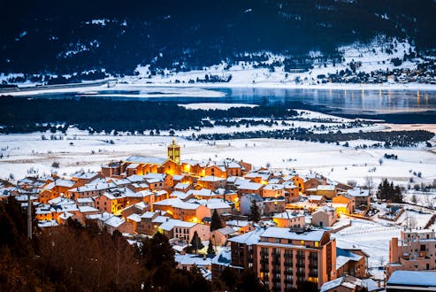 Le village de ski des Angles la nuit, entouré de montagnes enneigées et de verdure, où l'école de ski dispense des cours de ski.