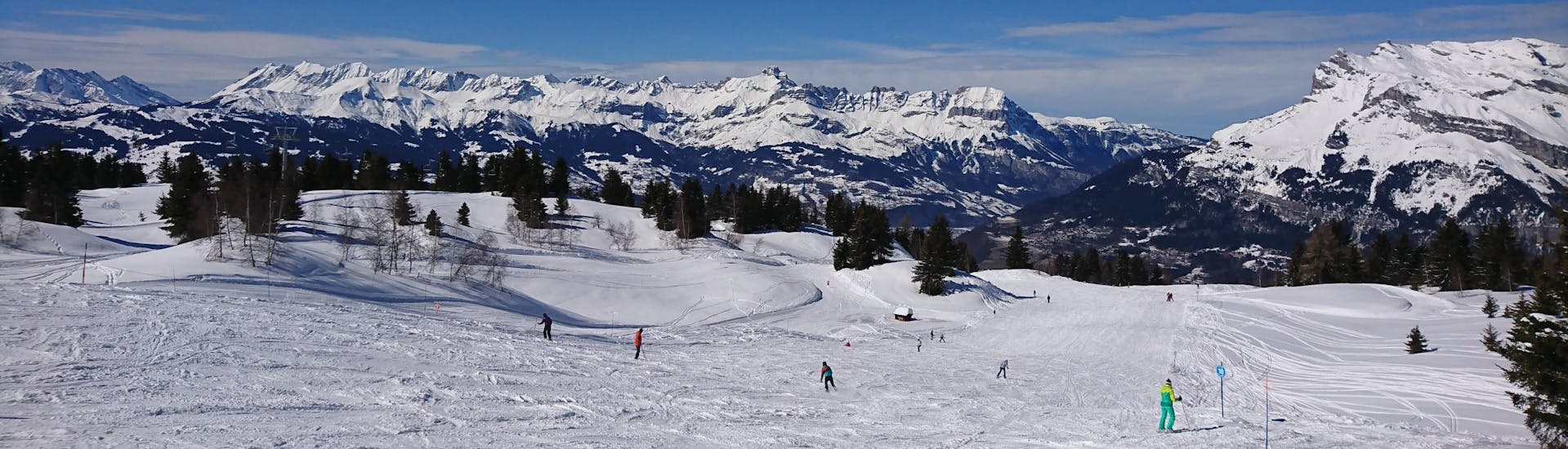 Vue panoramique de la station de ski des Houches avec un ciel bleu clair où les skieurs prennent des cours de ski dans les écoles de ski.
