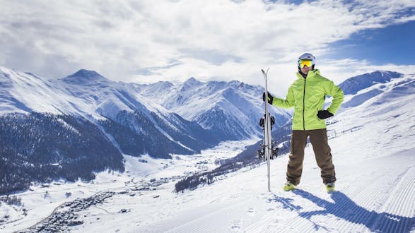 A skier is posing on one of the ski slopes in Livigno, overlooking the snow-covered ski resort from the top of the mountain.