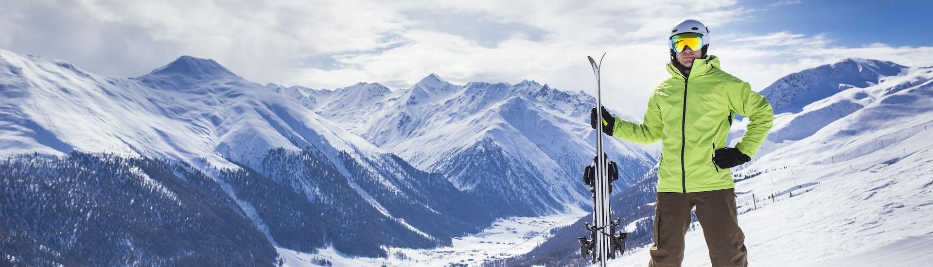 A skier is posing on one of the ski slopes in Livigno, overlooking the snow-covered ski resort from the top of the mountain.