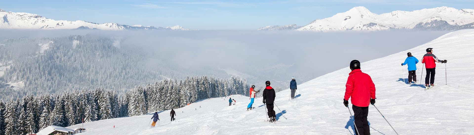 A number of skiers is skiing down a ski slope in the ski resort of Morzine, with a beautiful view of the surrounding mountainscape that is visible to all who book ski lessons with the local ski schools. 