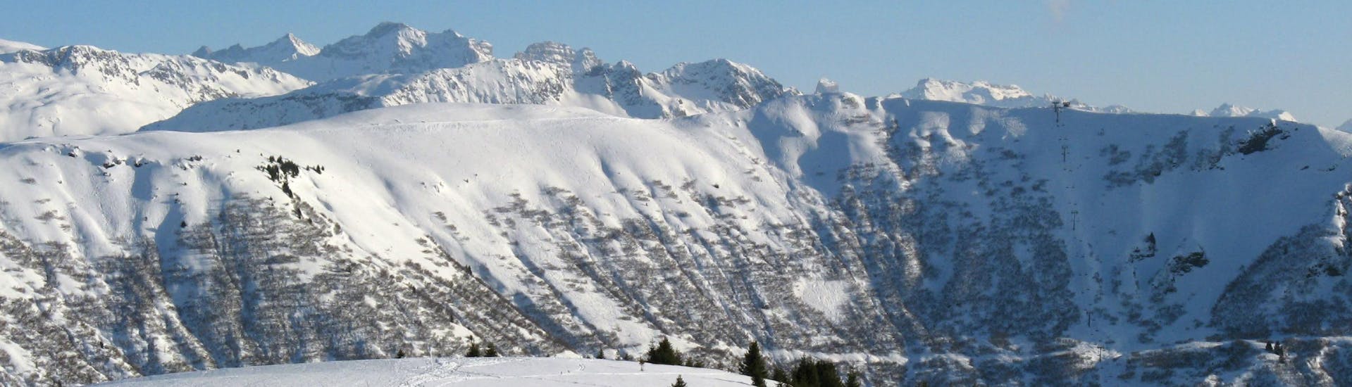 A picturesque view of ski slopes of Notre Dame de Bellecombe, a French ski resort nestled between the majestic peaks of the Savoy department, where local ski schools offer a broad range of ski lessons for anyone who wishes to learn to ski.