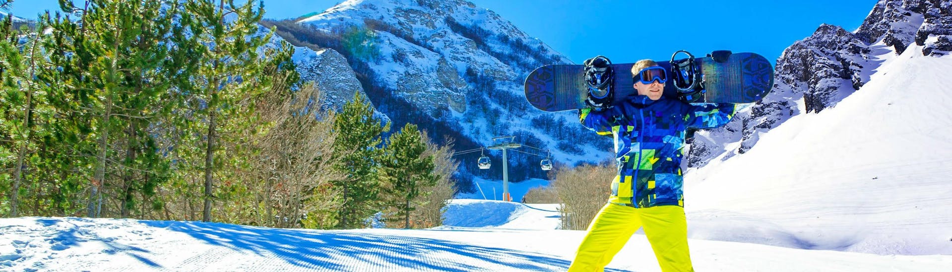 Uno snowboarder sta sorridendo alla fotocamera su una pista soleggiata del comprensorio sciistico di Ovindoli, dove è possibile scegliere tra un'ampia gamma di corsi di sci e snowboard offerti dalle scuole di sci locali.
