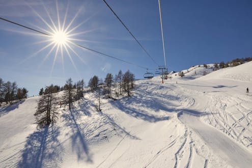 The sun is shining on a ski lift and the snowy slopes of Pra Loup, where local ski schools offer their ski lessons.