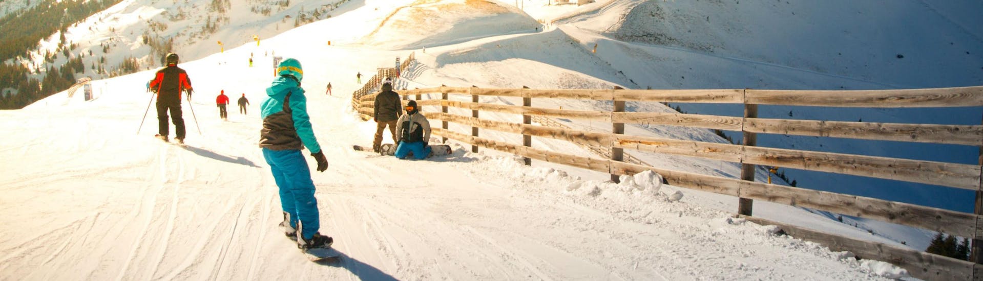 Eine Gruppe Skifahrer und Snowboarder fährt eine in Sonnenlicht getränkte Skipiste im Skigebiet Saalbach-Hinterglemm hinunter, wo örtliche Skischulen ihre Skikurse für die die das Skifahren lernen wollen anbieten.