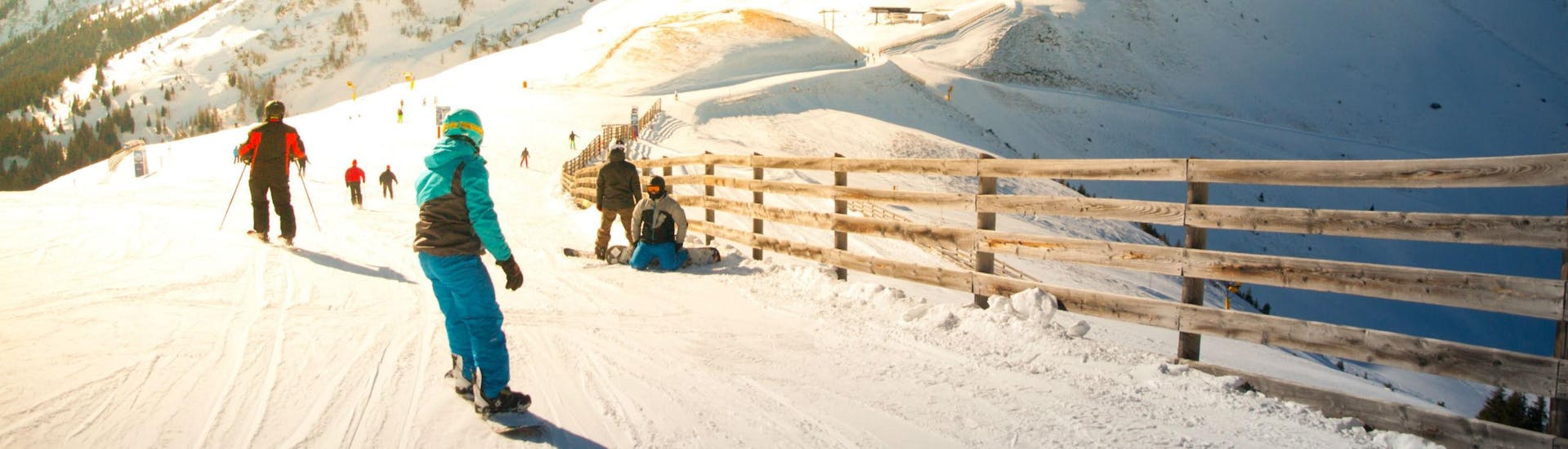 Eine Gruppe Skifahrer und Snowboarder fährt eine in Sonnenlicht getränkte Skipiste im Skigebiet Saalbach hinunter, wo örtliche Skischulen ihre Skikurse für die die das Skifahren lernen wollen anbieten.