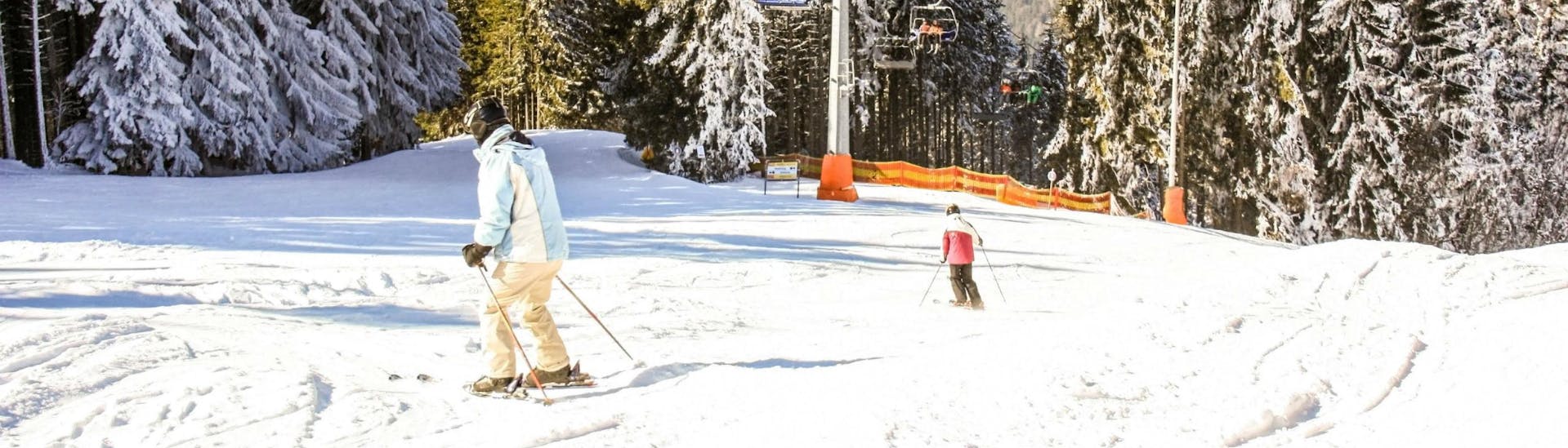 Zwei Skifahrer fahren nacheinander die Skipiste im Skigebiet Semmering hinunter, wo Besucher bei den örtlichen Skischulen eine Reihe an Skikursen buchen können.