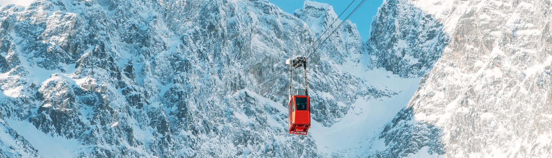 A red gondola going up to a peak in the ski resort Tatranská Lomnica in Slovakia, where local ski schools offer their ski lessons.