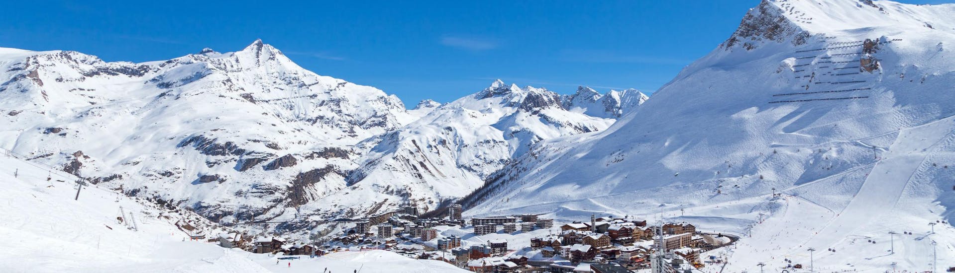 Une vue de la station de ski de Tignes sous un grand ciel bleu, avec ses nombreuses pistes utilisées par les écoles de ski locales pour leurs cours de ski.