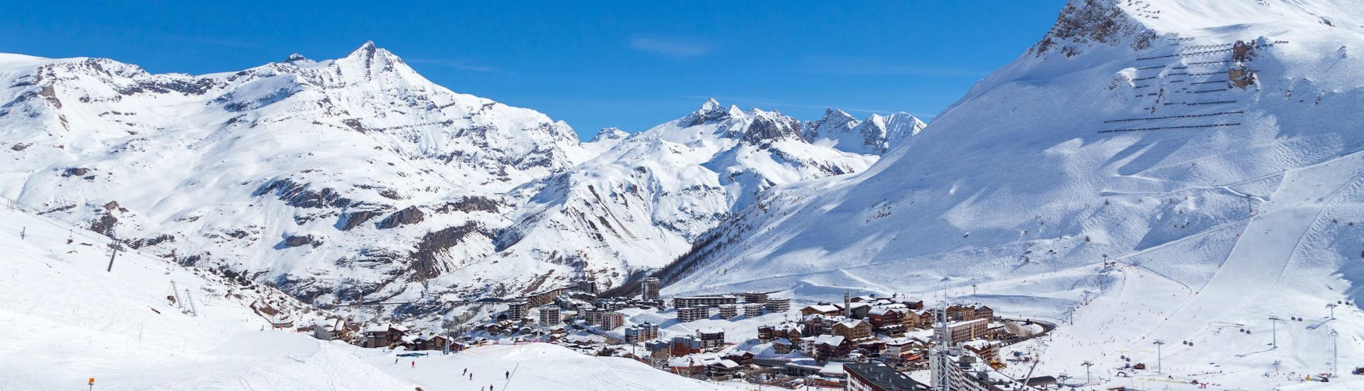 Une vue de la station de ski de Tignes sous un grand ciel bleu, avec ses nombreuses pistes utilisées par les écoles de ski locales pour leurs cours de ski.