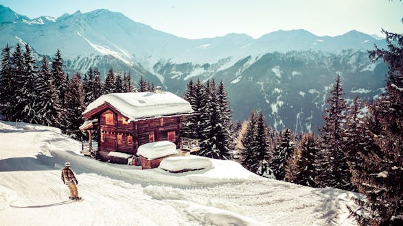 An image of a lone snowboarder boarding past a small mountain hut in the swiss ski resort of Verbier, where where visitors can learn to ski during their ski lessons provided by local ski schools.