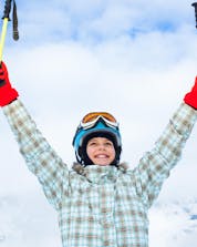 Una joven está levantando sus bastones de esquí al aire, emocionada por sus clases de esquí con una de las escuelas de esquí de Alto Campo.
