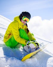 Eine Snowboarderin sitz auf der Skipiste in Schönried-Saanenmöser-Zweisimmen, wo örtliche Skischulen ihre Skikurse durchführen.