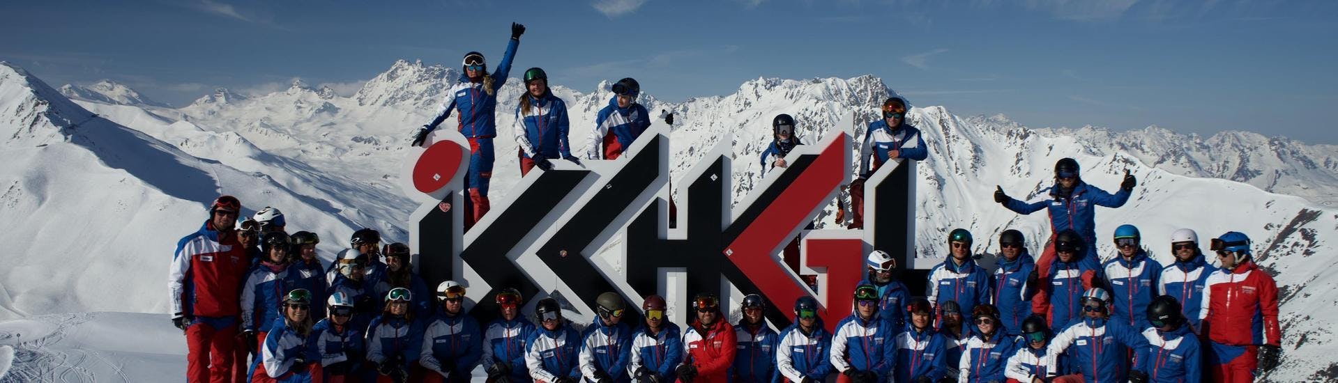 The ski instructors from Skischule Ischgl Schneesport Akademie are gathered around the logo of the ski school and are seemingly looking forward to teaching their ski lessons.