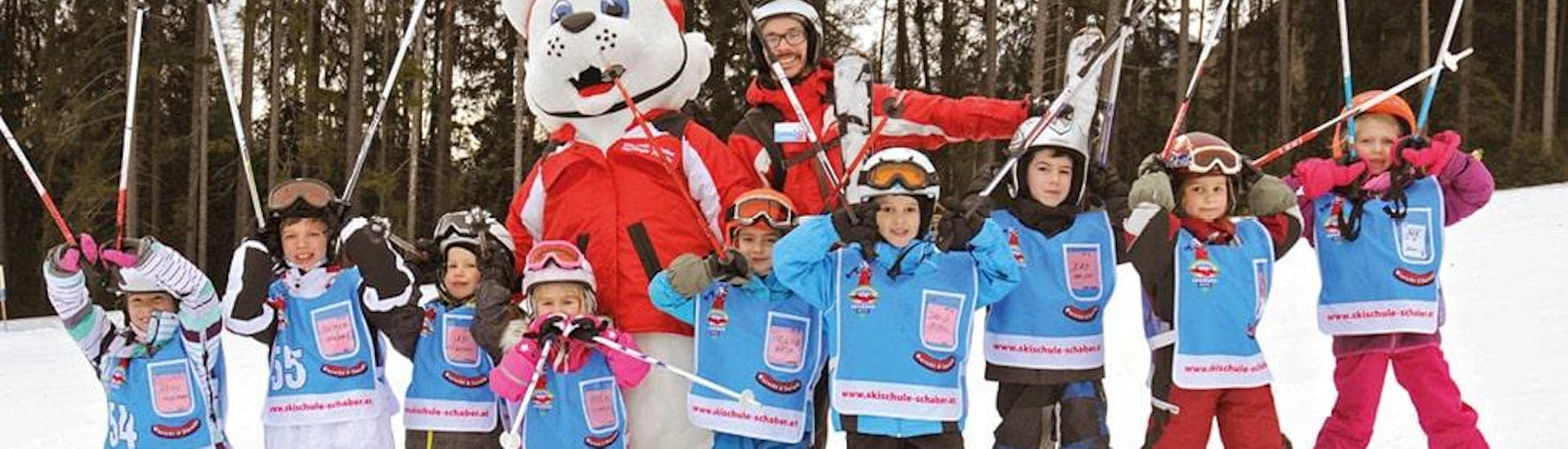 A group of children is posing for a photo with their ski instructor from Skischule Schaber in Grünberg Obsteig and the ski school mascot Hermi Hermelinchen during one of their ski lessons.