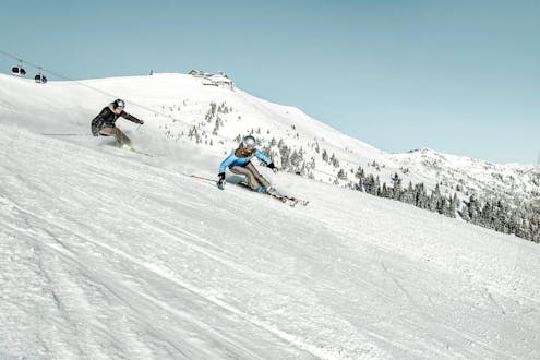 Zwei Skifahrer carven die Skipiste auf der Schmittenhöhe in Zell am See hinunter, wo örtliche Skischulen ihre Skikurse sowohl für Anfänger als auch Fortgeschrittene anbieten.