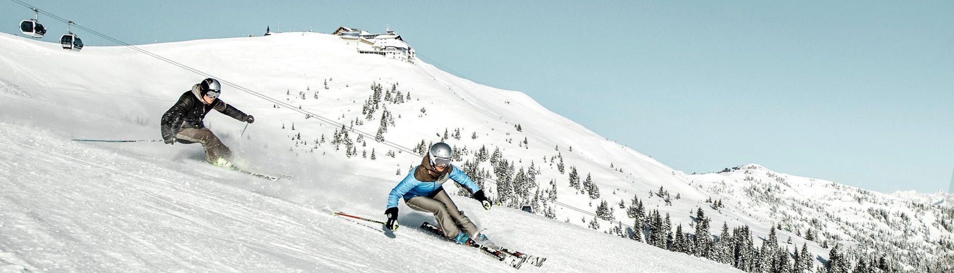 Two skiers are skiing down the ski slopes of the Schmittenhöhe mountain in Zell am See, a popular Austrian ski resort where local ski schools offer ski lessons to all those who want to learn to ski.