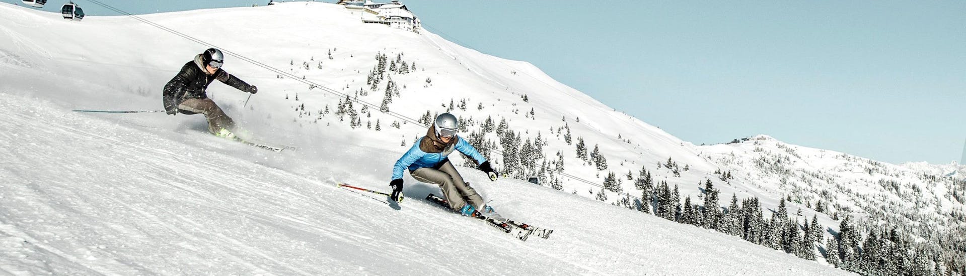 Two skiers are skiing down the ski slopes of the Schmittenhöhe mountain in Zell am See, a popular Austrian ski resort where local ski schools offer ski lessons to all those who want to learn to ski.