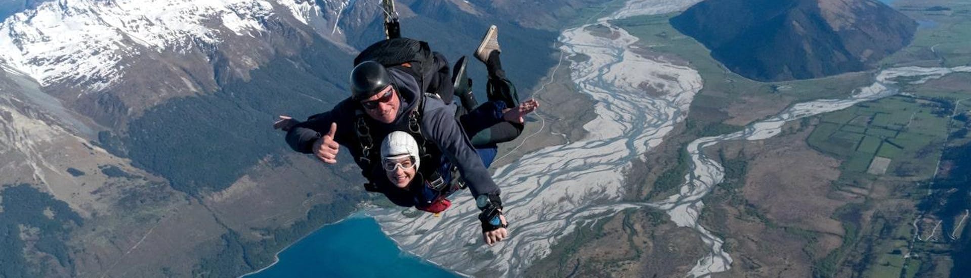 A tandem master from Skydive Southern Alps Queenstown and his passenger are smiling at the camera as they skydive over the Dart River estuary near Glenorchy.