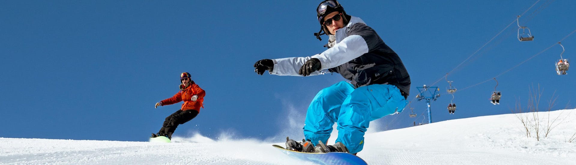 Two snowboarders are racing down a freshly prepared slope during their snowboarding lessons.
