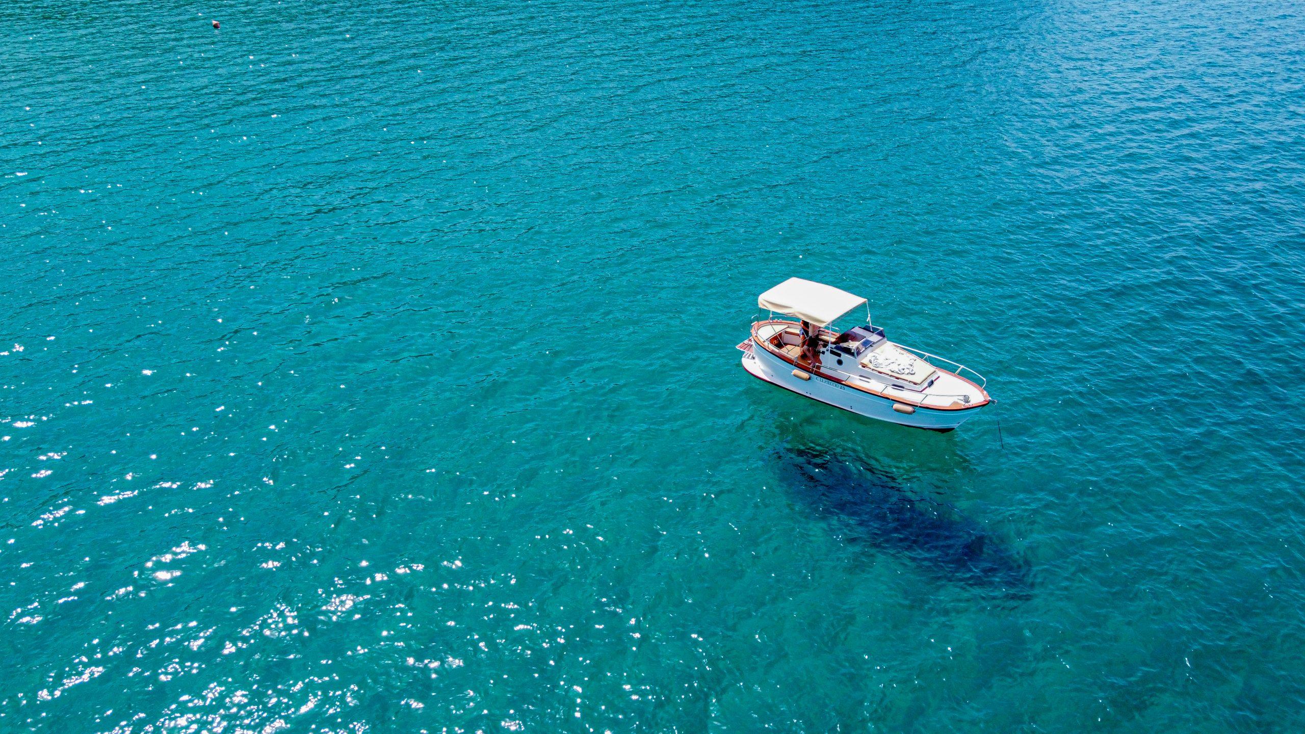 Boat anchored in the clear turquoise waters of Cala Violina, Tuscany.
