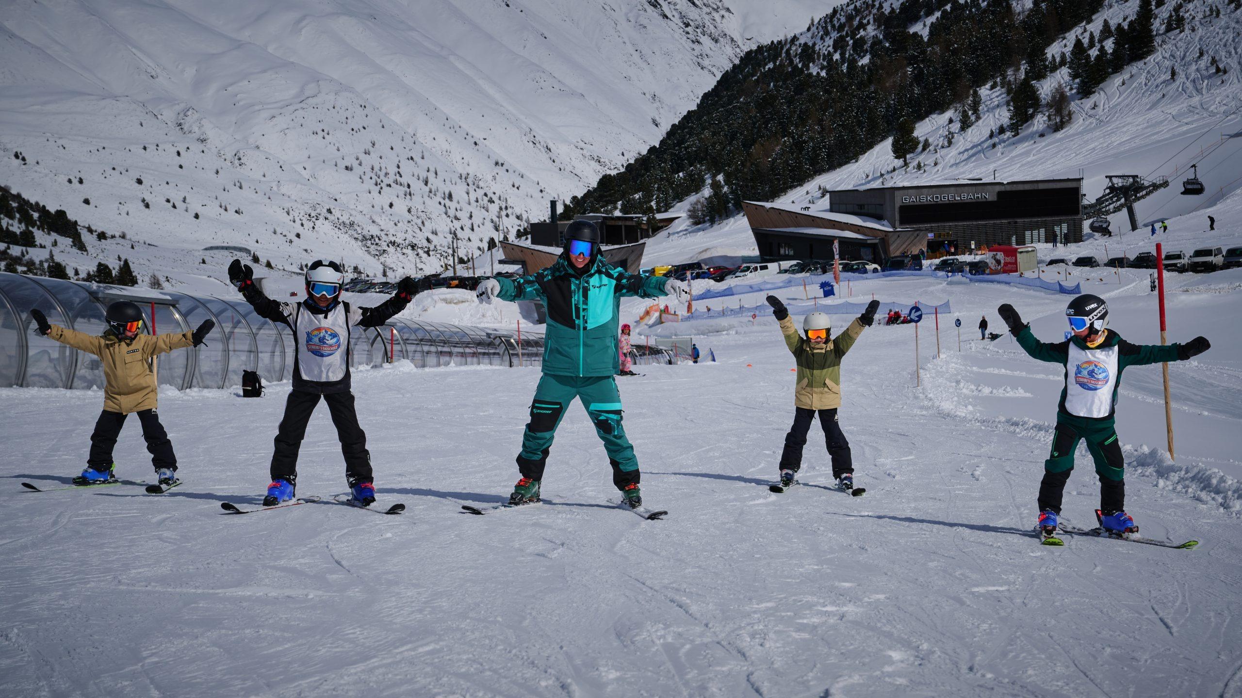 Skilehrer mit vier Kindern bei einer Skistunde an einem sonnigen Tag auf den verschneiten Pisten.