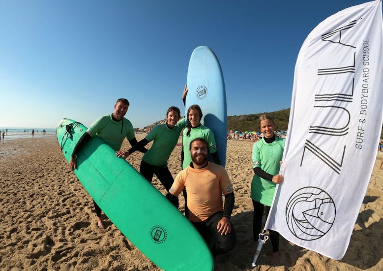 Un gruppo di persone in spiaggia che sorridono e si divertono durante le lezioni di surf a Nazaré con Zulla Surf School Nazaré.