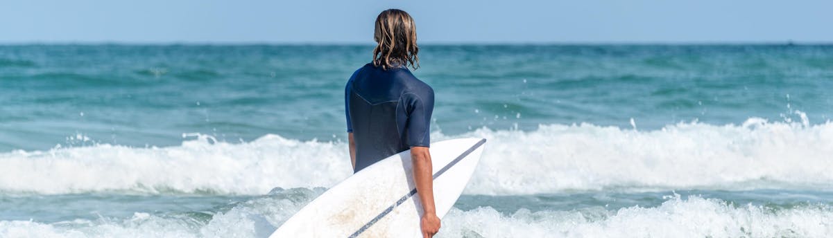 surfing-arcachon_SEM-Resort-Hero An image of a surfer stood knee-deep in the ocean as he gets ready to go surfing in Arcachon.