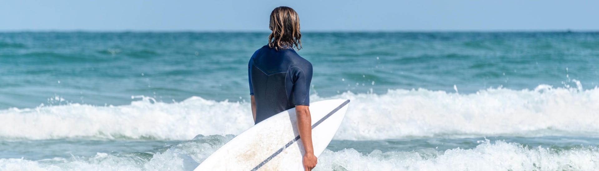 Une photo d'un surfeur debout jusqu'aux genoux au milieu des vagues qui s'apprête à surfer à Arcachon.
