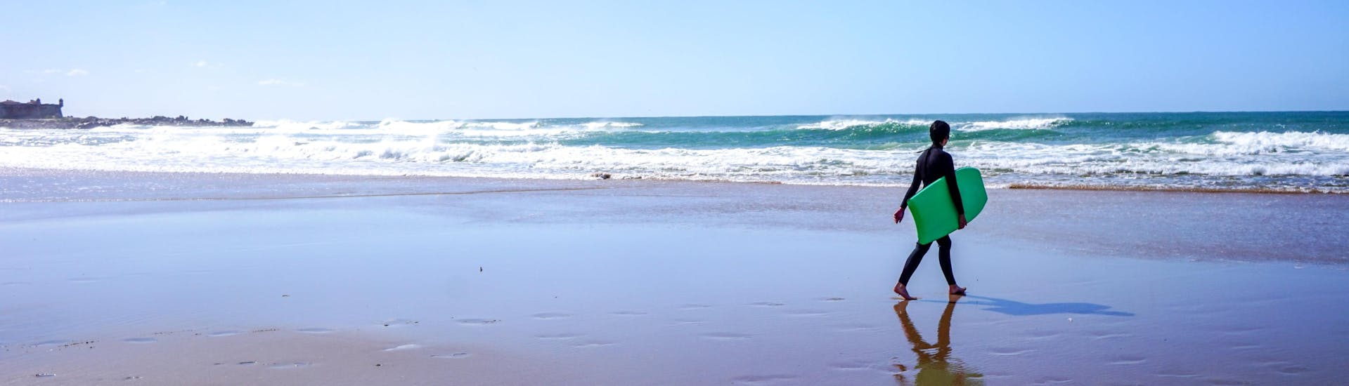 Una joven es fotografiada caminando por la playa con su tabla mientras surfea en Porto.