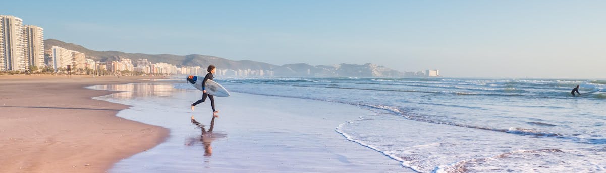surfing-valencia_SEM-Resort-Hero A young man is running towards the ocean while surfing in Valencia.