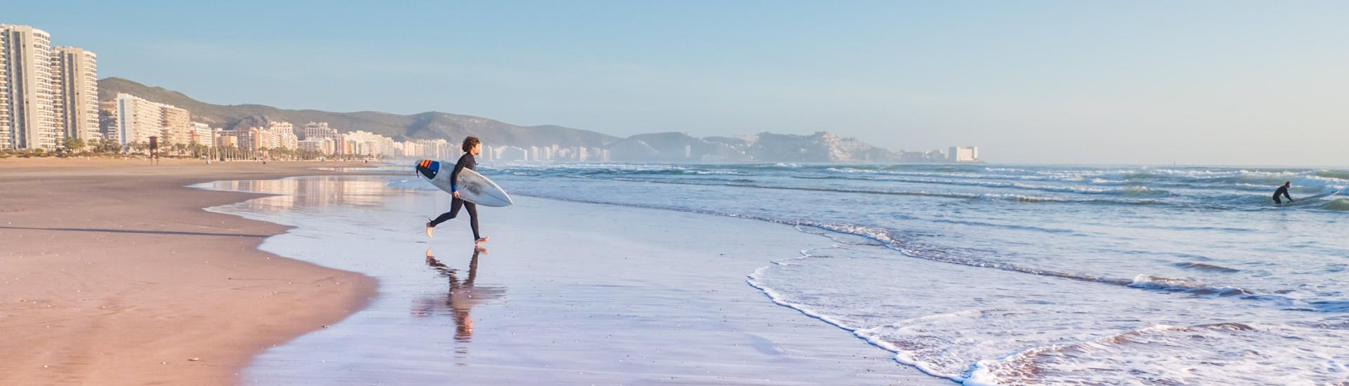 Ein junger Mann läuft beim Surfen in Valencia den Wellen entgegen.