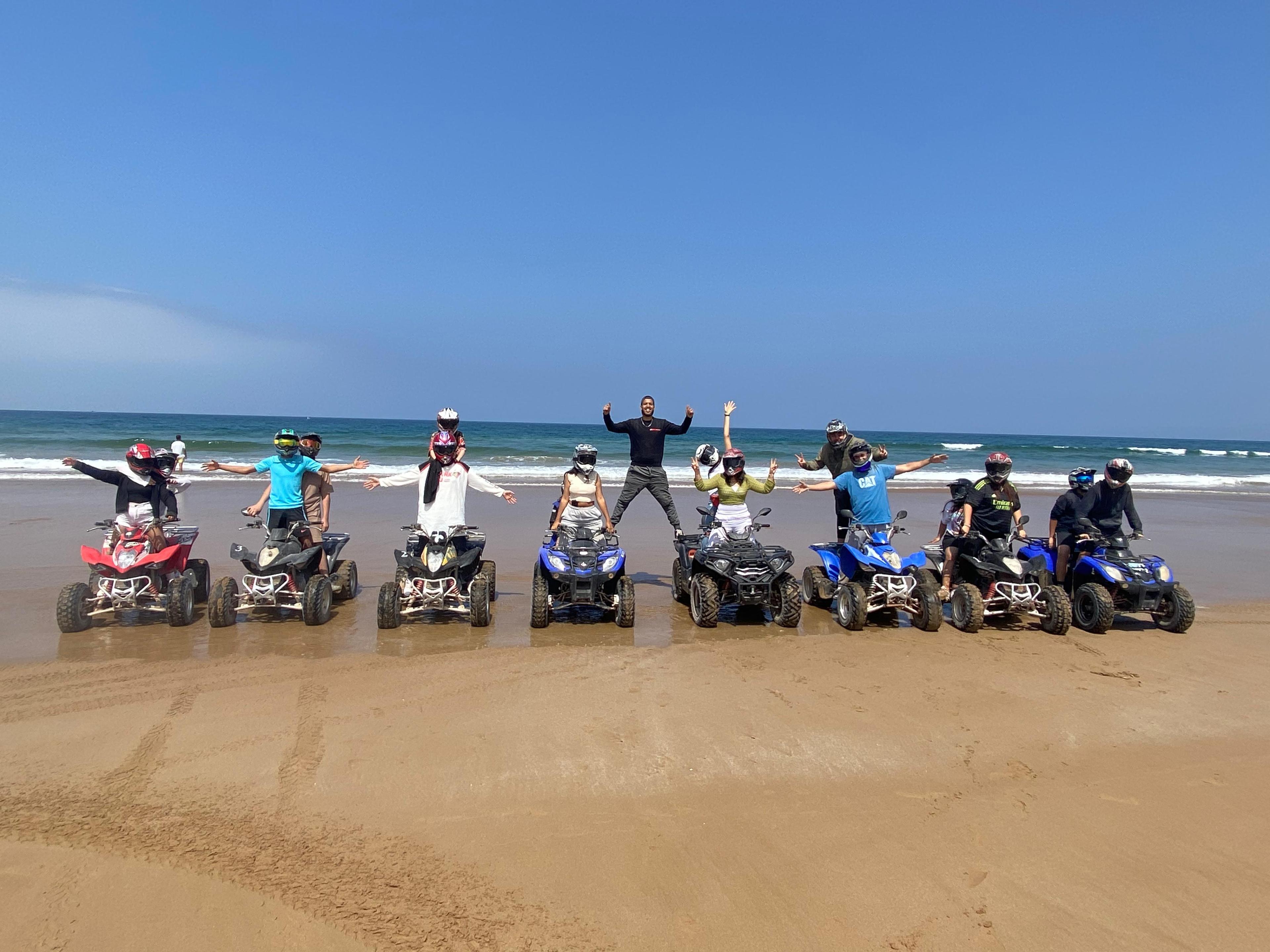 Un groupe de personnes en ligne sur la plage et sur leurs quads avec leurs casques, regardant la caméra avec les mains en l'air.